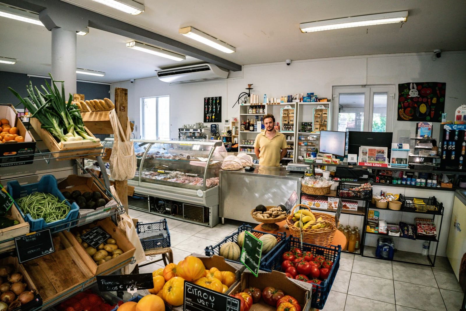 L'intérieur de l'épicerie L'Esquirol à Ceilhes : cagettes de fruits et légumes, comptoir et banc de charcuterie